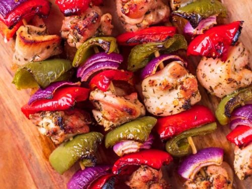 Four marinated chicken skewers on a wooden board.