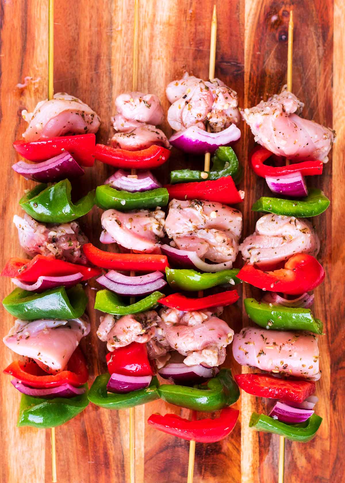 Raw chunks of chicken and chopped peppers and onion threaded onto four bamboo skewers.