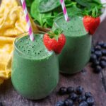 Two glasses of super green smoothie with a strawberry on the glass rim.