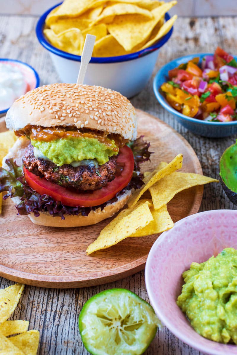 A burger in a sesame seed bun with tomato and guacamole.