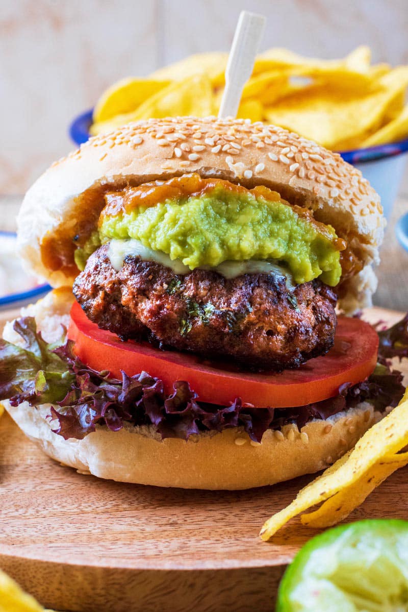 Mexican burger in a bun with sliced tomato, lettuce and avocado.