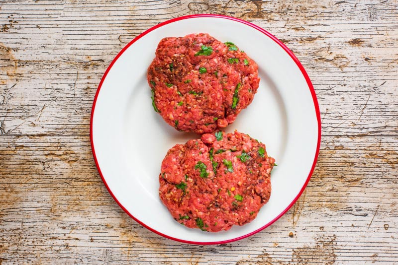 Two raw burger patties on a white plate.