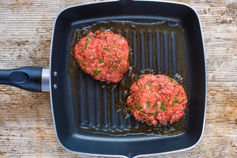 Two burger patties cooking in a griddle pan.