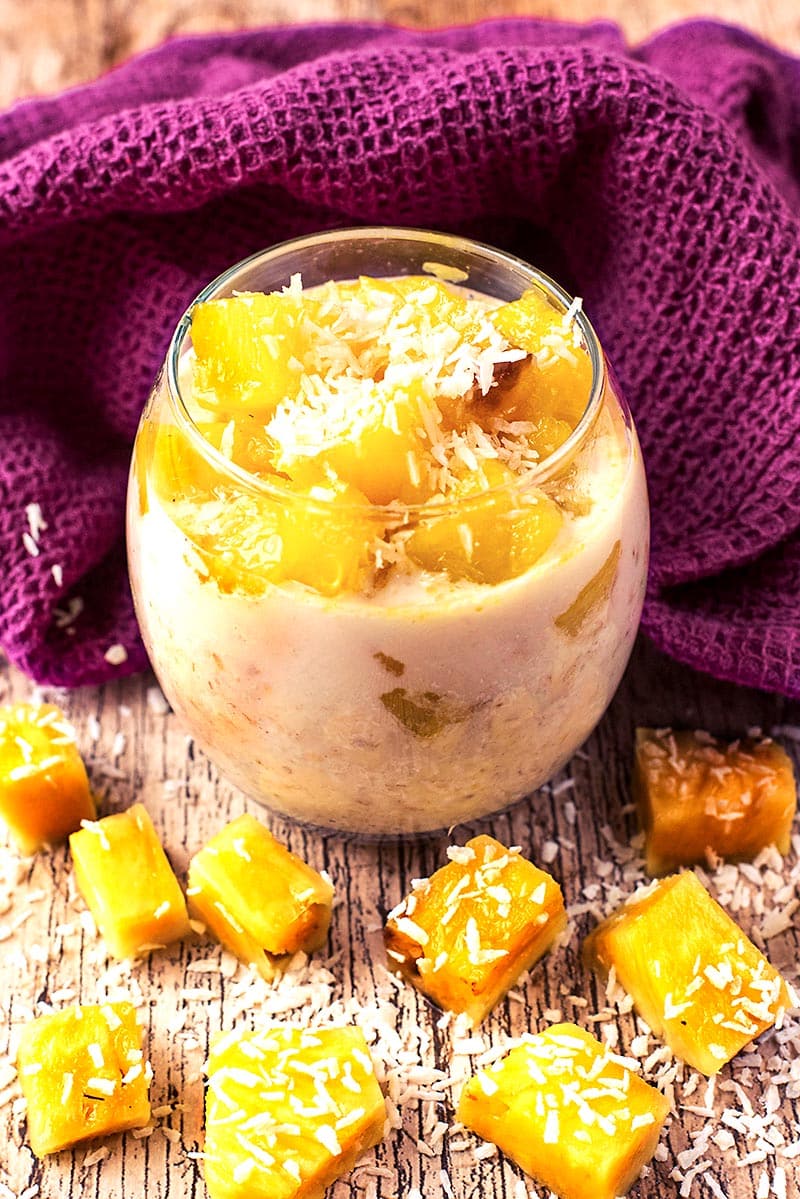A glass of overnight oats topped with chunks of pineapple and shredded coconut.
