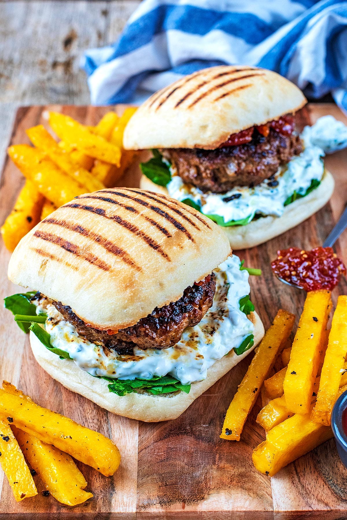 Two Spiced Lamb Burgers on a wooden board with fries and dip.