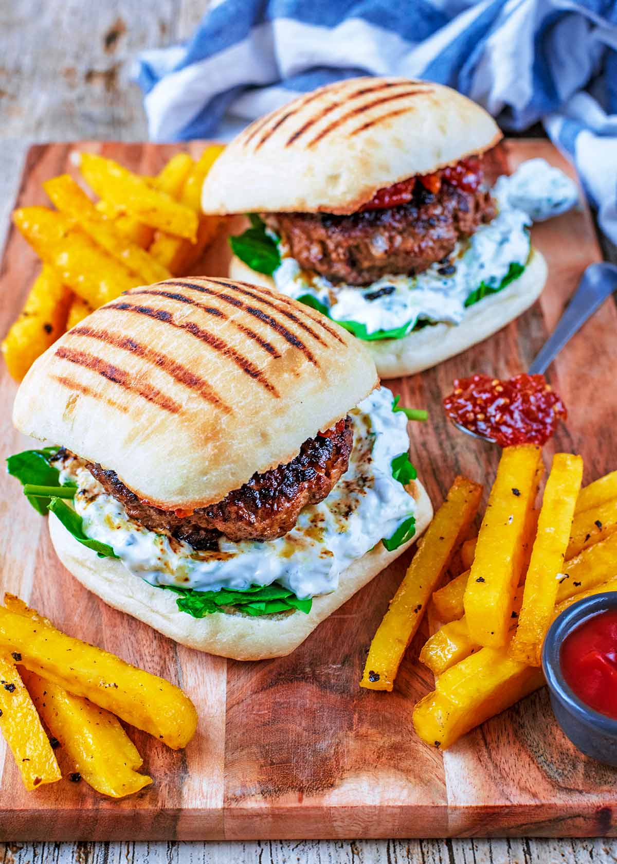 Two lamb burgers in ciabatta buns on a wooden board with fries and dip.