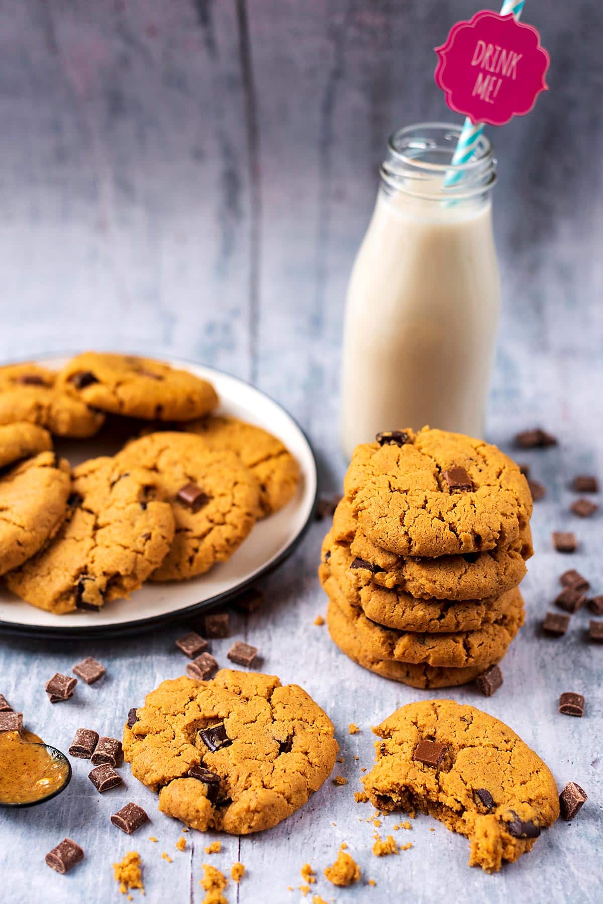 A plate of chocolate chip cookies next to a stack of more cookies and a bottle of milk