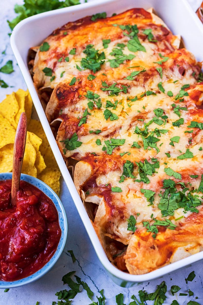 A dish of enchiladas next to some chips and salsa.