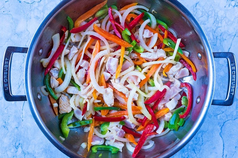 A large pan with chopped vegetables and chunks of chicken cooking in it.
