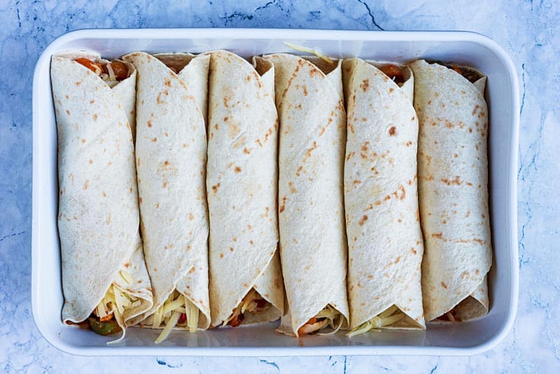Six rolled up enchiladas in a baking dish.