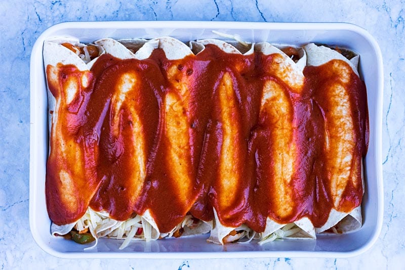 A baking dish with six enchiladas covered in sauce.