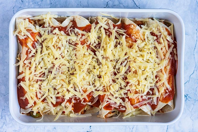 Enchiladas in a baking dish covered in sauce and cheese.