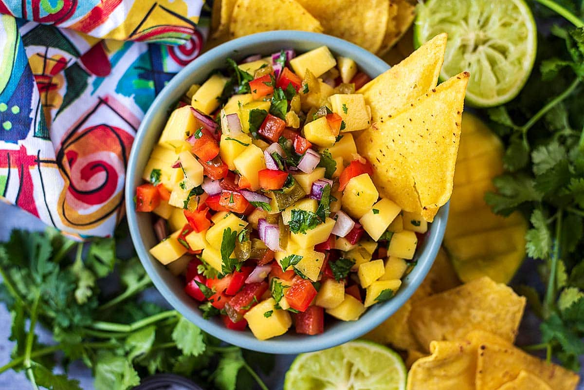 A bowl of mango salsa with some tortilla chips in it.