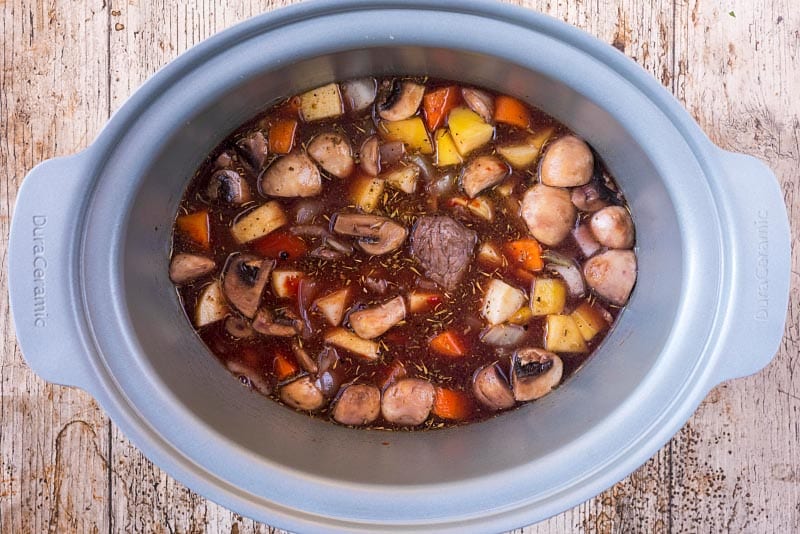A Crock Pot bowl containing chunks of beef, chopped vegetables and gravy.