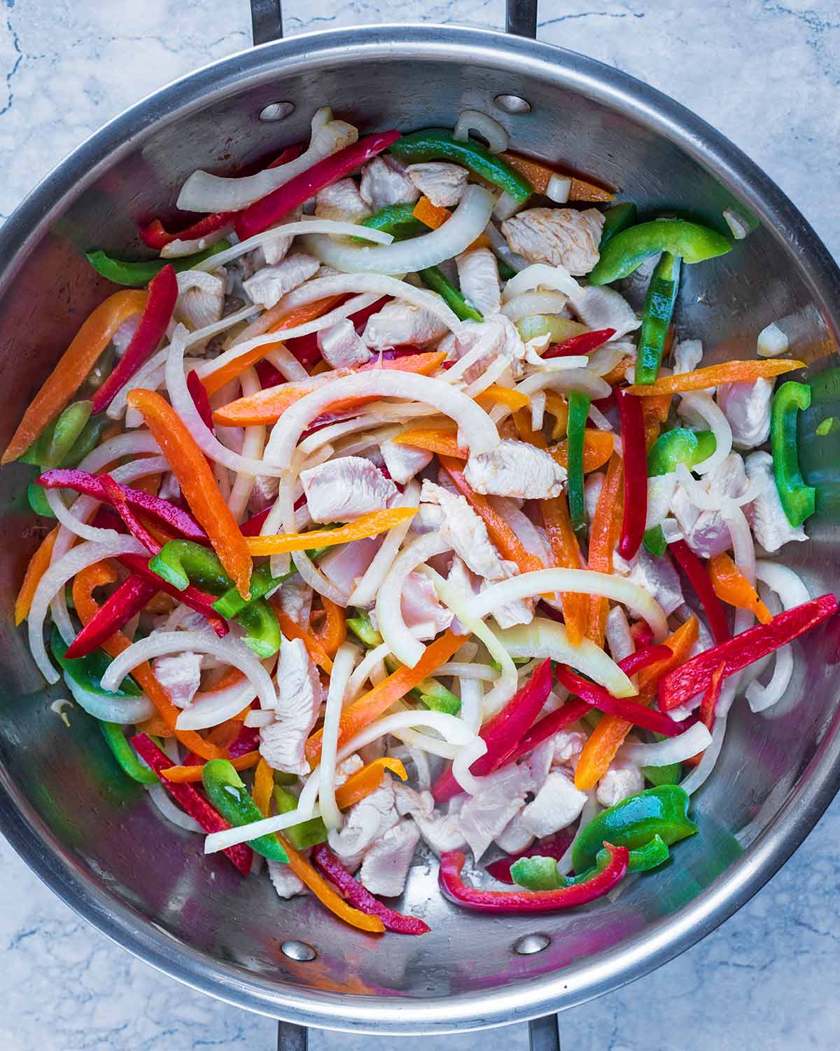 A large pan with chopped vegetables and chunks of chicken cooking in it.