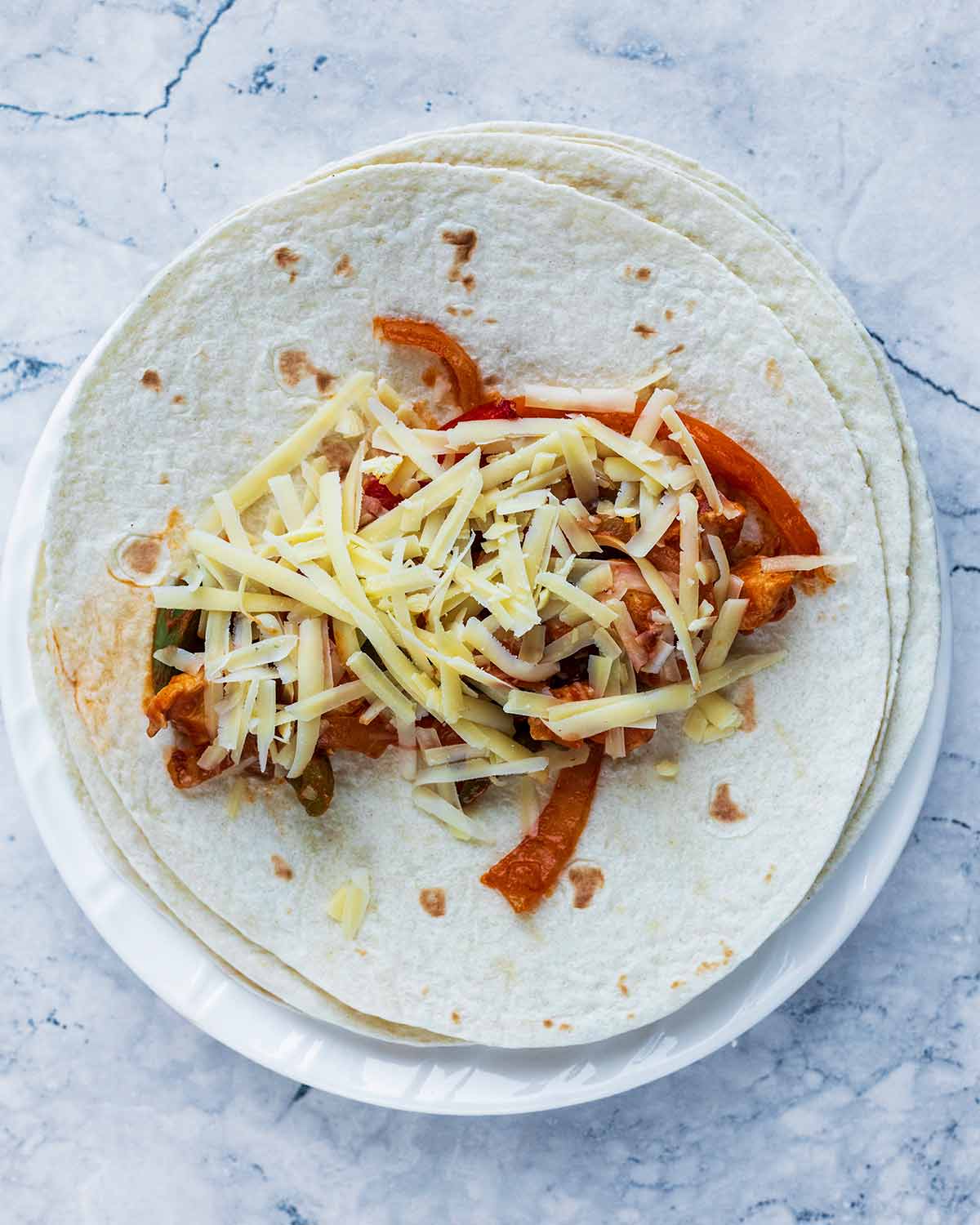 A flour tortilla with enchilada filling and cheese on it.