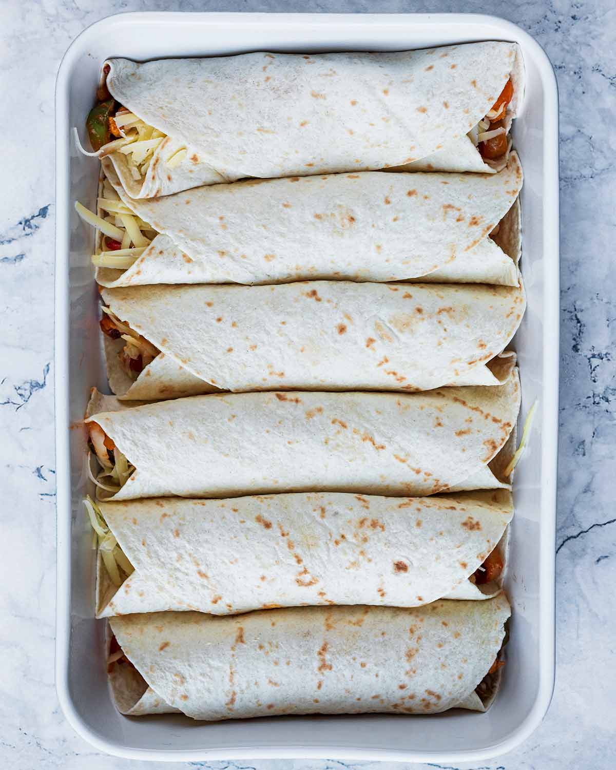 Six rolled up enchiladas in a baking dish.
