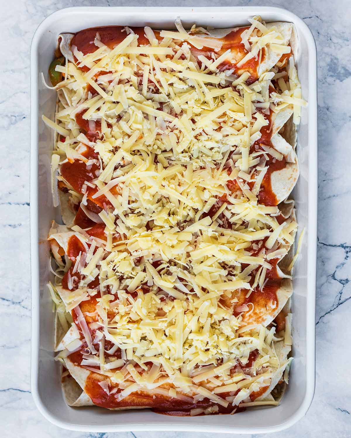 Enchiladas in a baking dish covered in sauce and cheese.