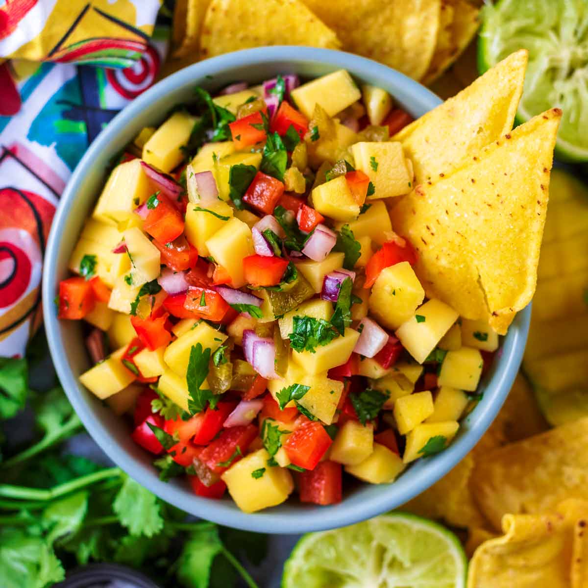 A blue bowl of mango salsa with two tortilla chips stuck in it.