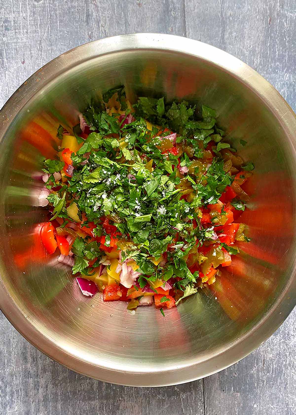 A metal mixing bowl containing chopped, mango, red pepper, onion and coriander.
