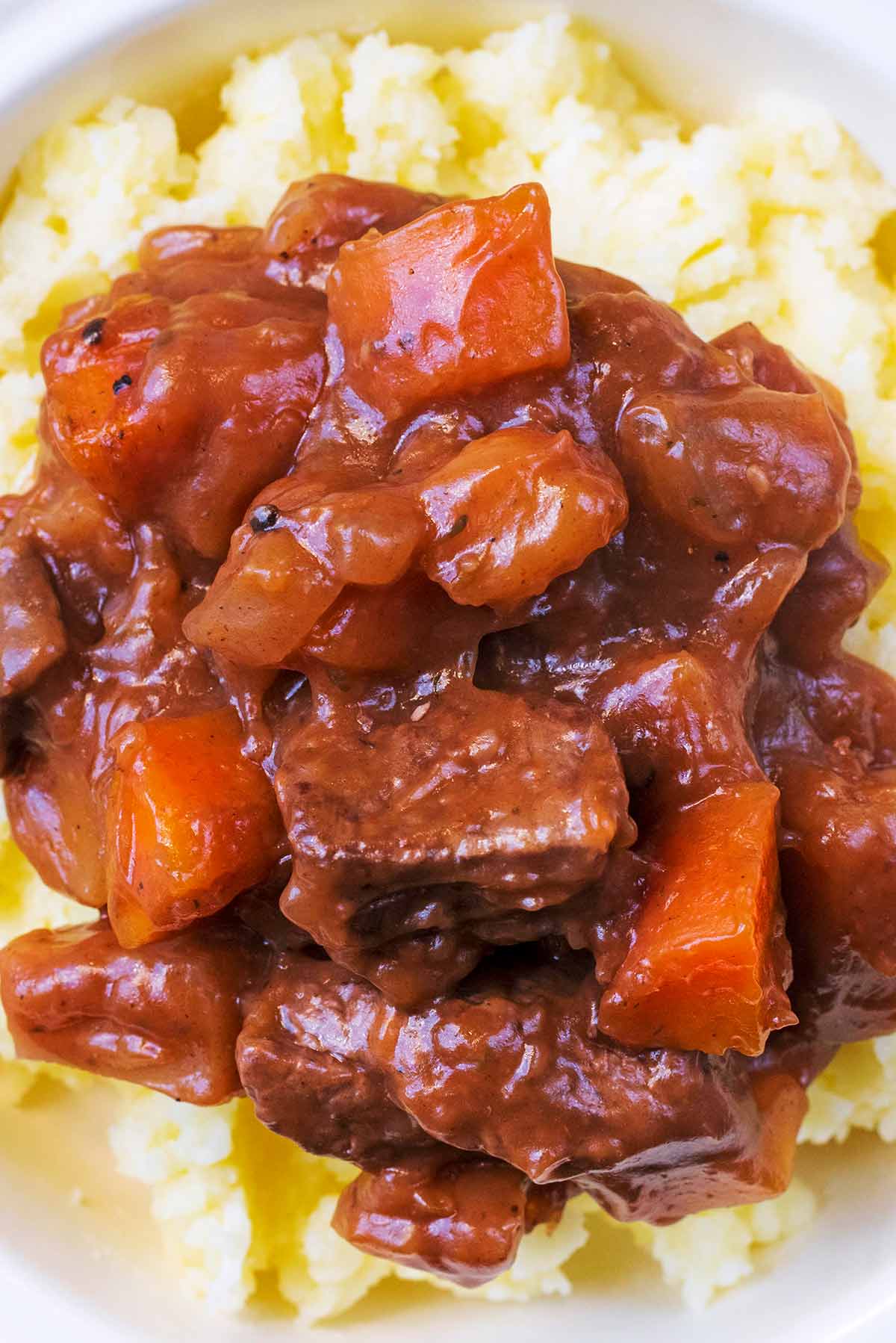 Chunks of cooked beef and chopped vegetables in a gravy sauce on top of mashed potato.