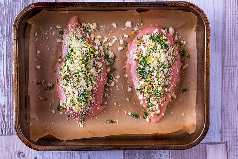 Stuffed chicken breasts coated in a herb crust in a baking tray.