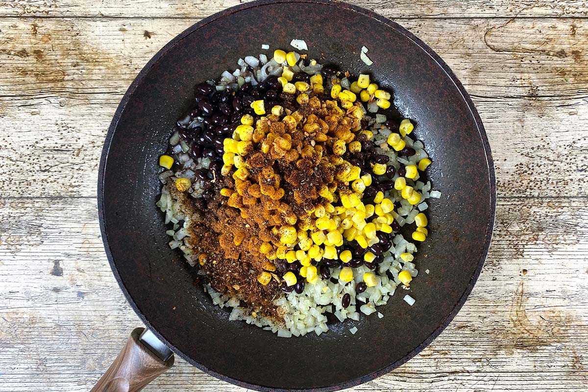 Onions, sweetcorn and black beans cooking in a frying pan.