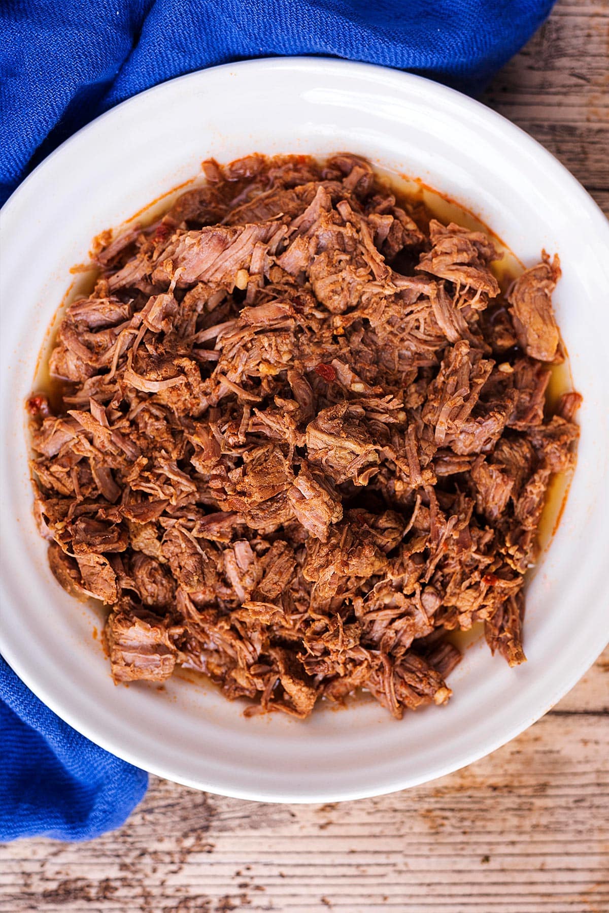 A bowl of pulled beef next to a blue towel.