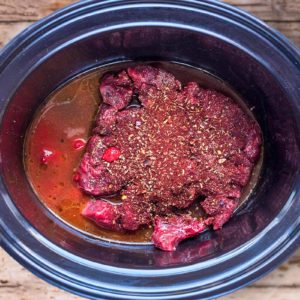 A slow cooker bowl containing beef, stock and spices