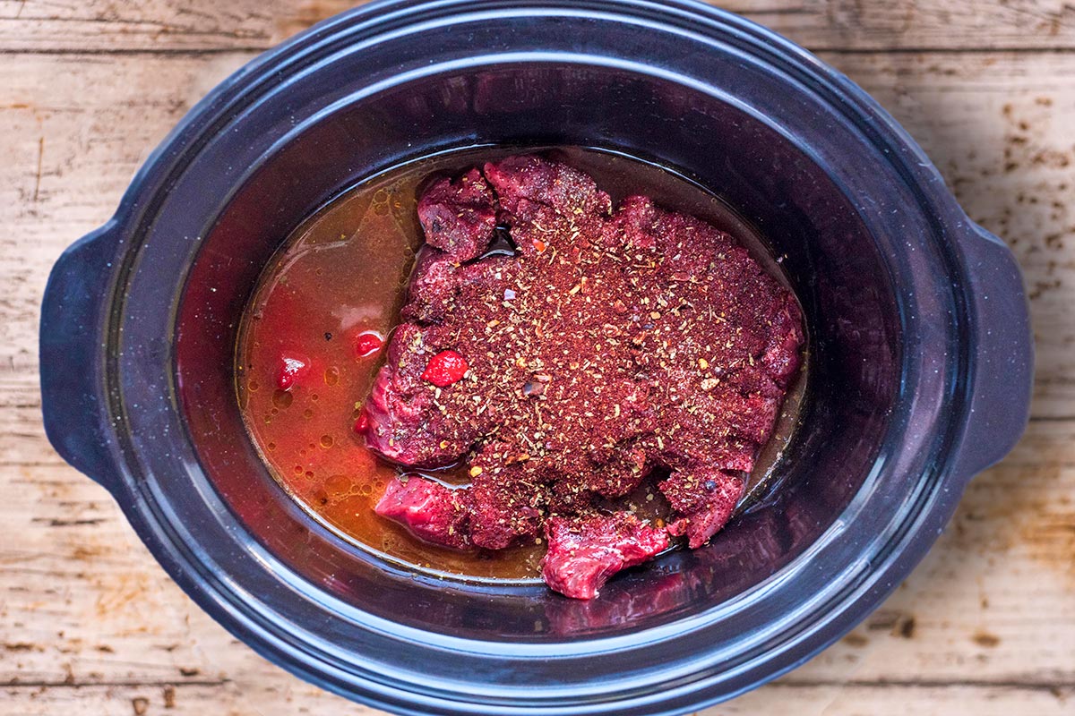 A slow cooker bowl containing beef, stock and spices.
