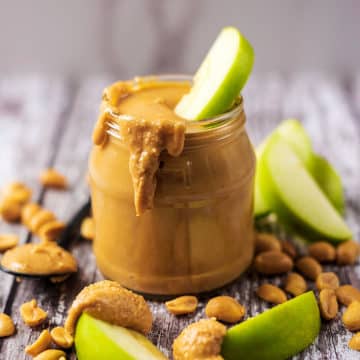 A jar of homemade peanut butter with slices of apple and peanuts