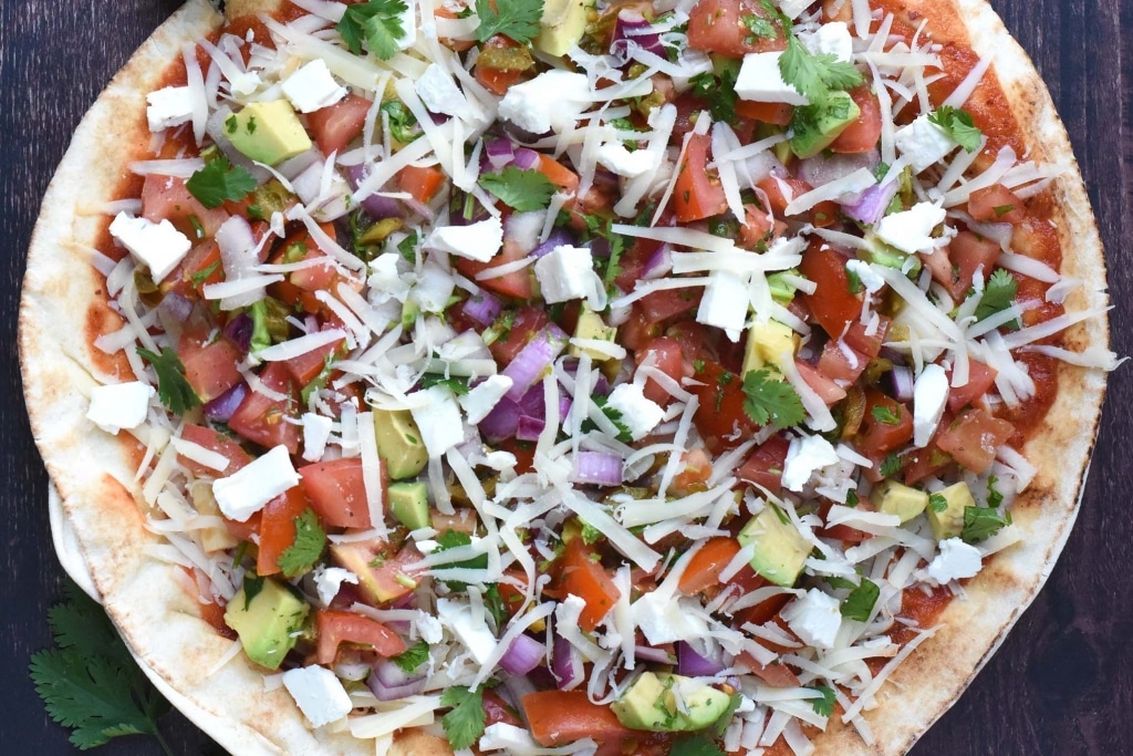 A pizza with tomato, avocado, onion, cheese and herbs