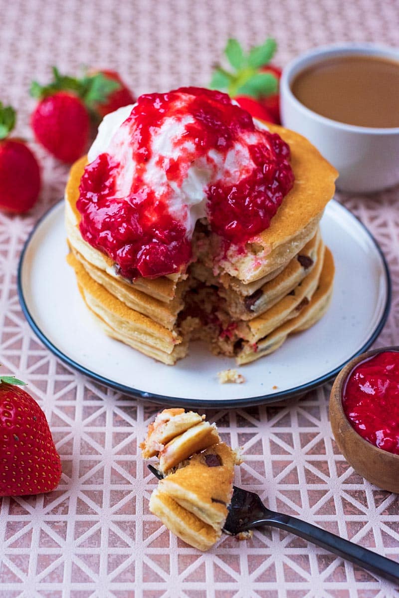 A stack of pancakes topped with cream and strawberry puree.