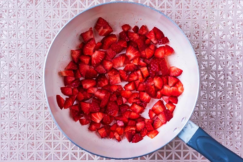 A saucepan with small chunks of strawberry in it.