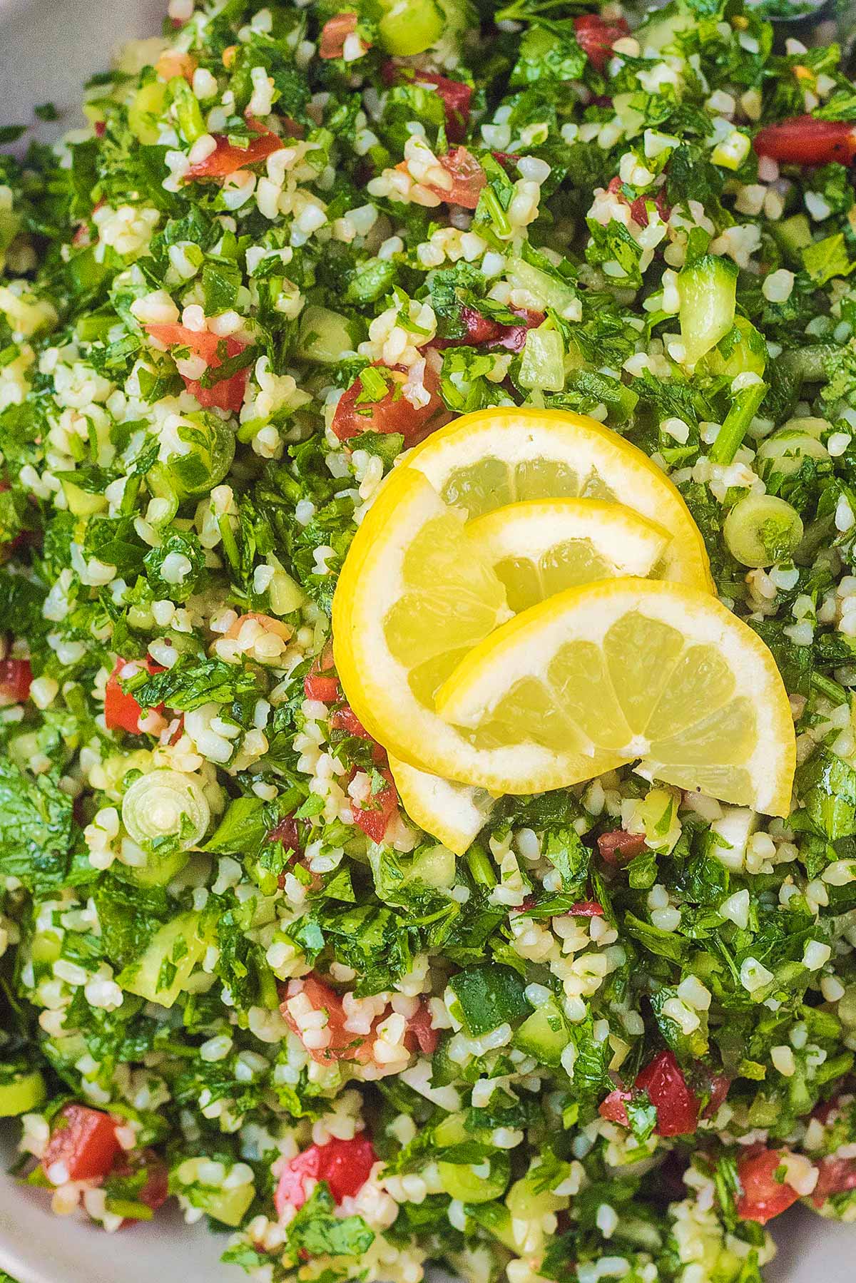 Four lemon slices on top of a serving of tabbouleh.