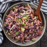 A bowl of broccoli slaw with a wooden serving spoon.