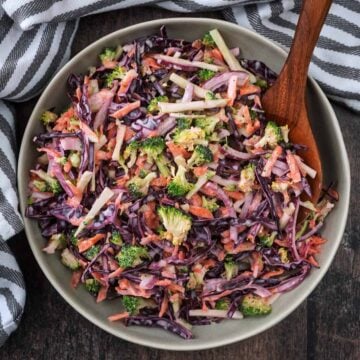 A bowl of broccoli slaw with a wooden serving spoon.