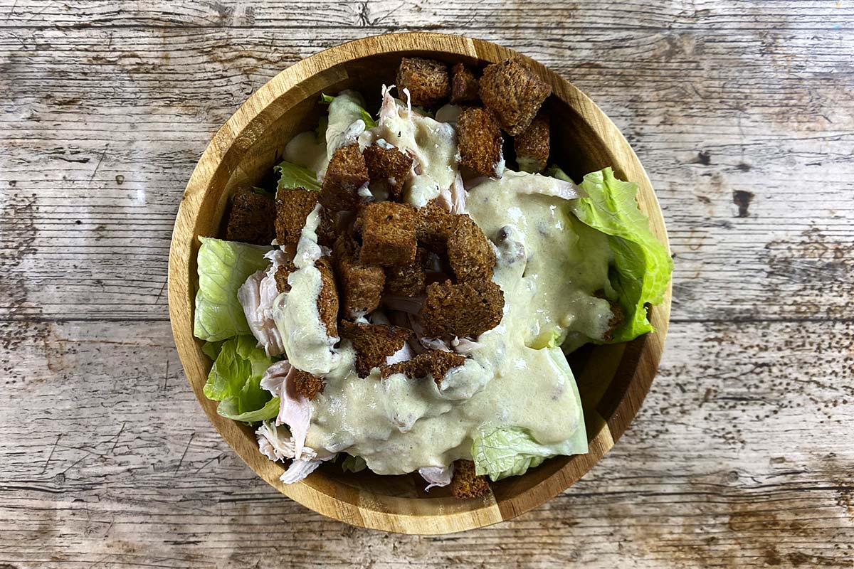 Chopped lettuce, croutons and chopped chicken in a bowl covered in caesar dressing.