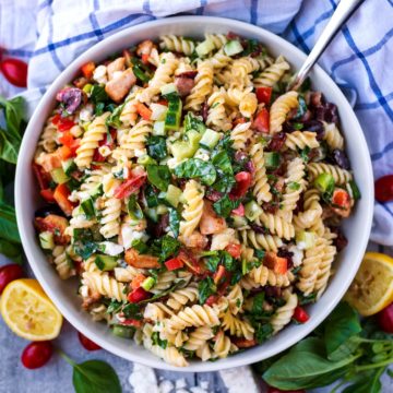 Chicken Pasta Salad in a large round bowl surrounded by lemon, cheese and basil leaves