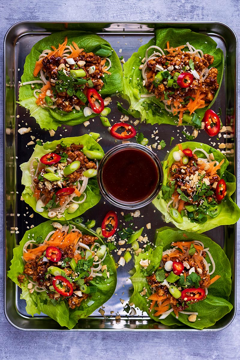 A large metal tray with six chicken lettuce wraps and a bowl of sauce