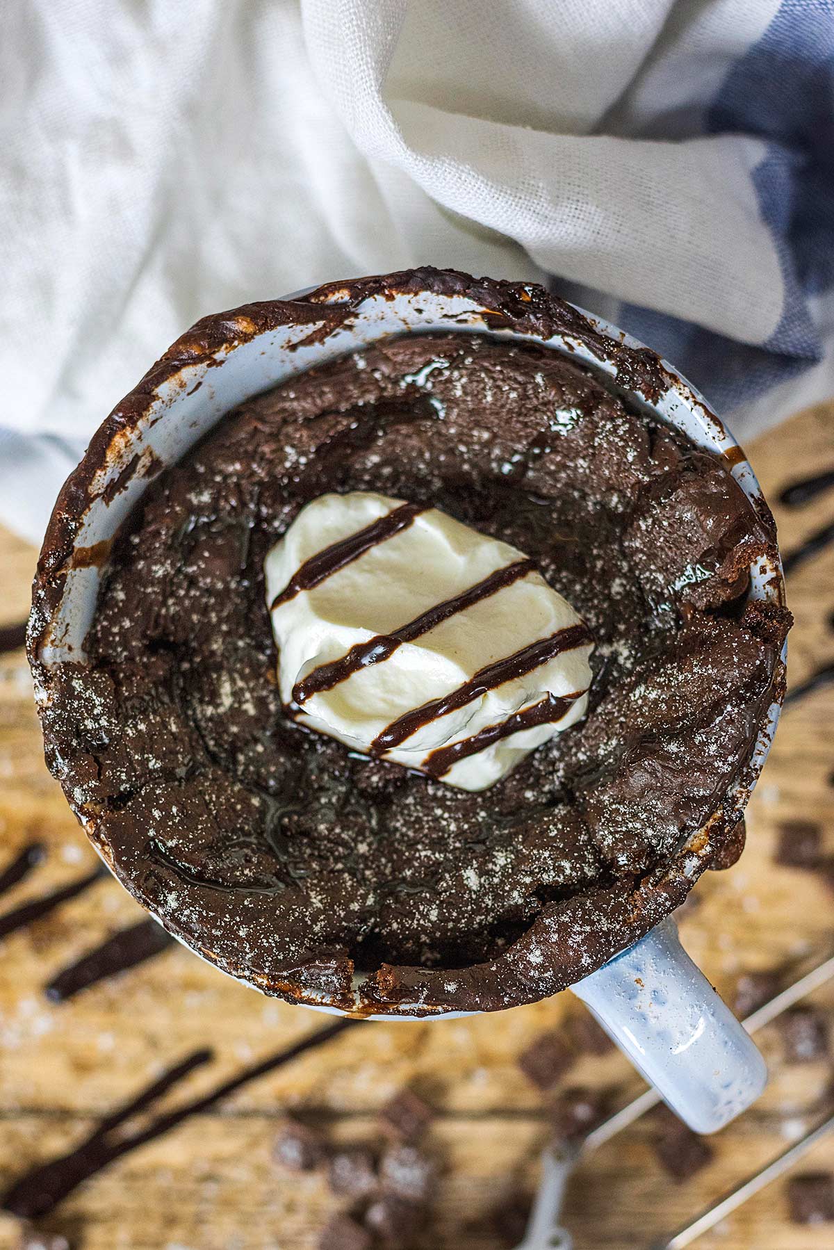 a chocolate cake in a mug topped with yogurt and a drizzle of chocolate.