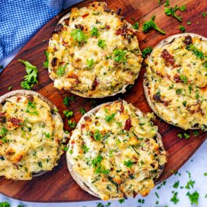 Four stuffed portobello mushrooms on a wooden board.