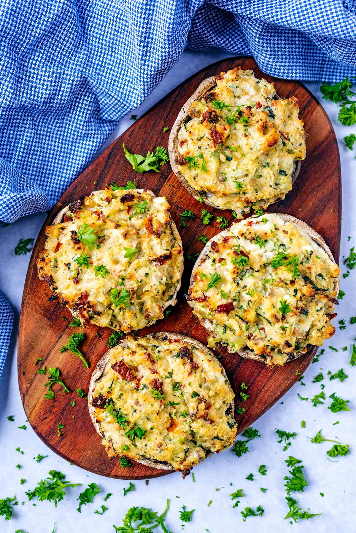 Four stuffed mushrooms on a wooden serving board.