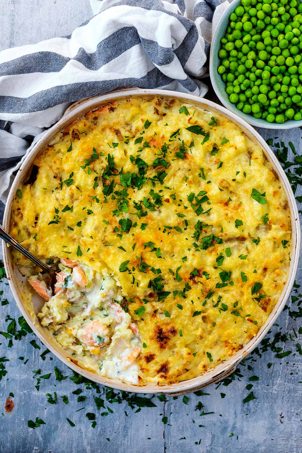 A large dish containing fish pie next to a bowl of peas.