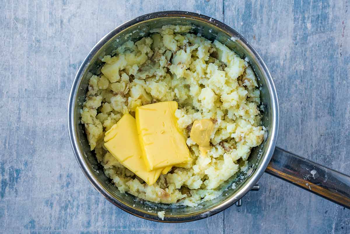 Mashed potatoes in a pan with pats of butter and a small dollop of mustard.