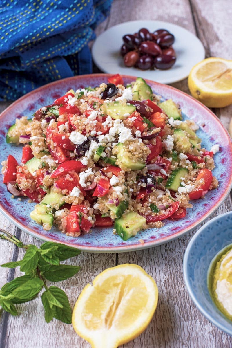 A plate of Quinoa Greek Salad with a half lemon sat in front of it.