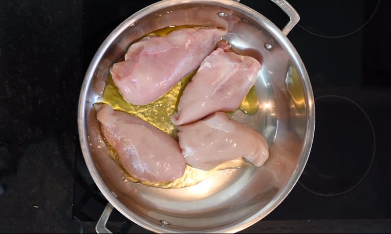 Four uncooked chicken breasts in a large silver pan.