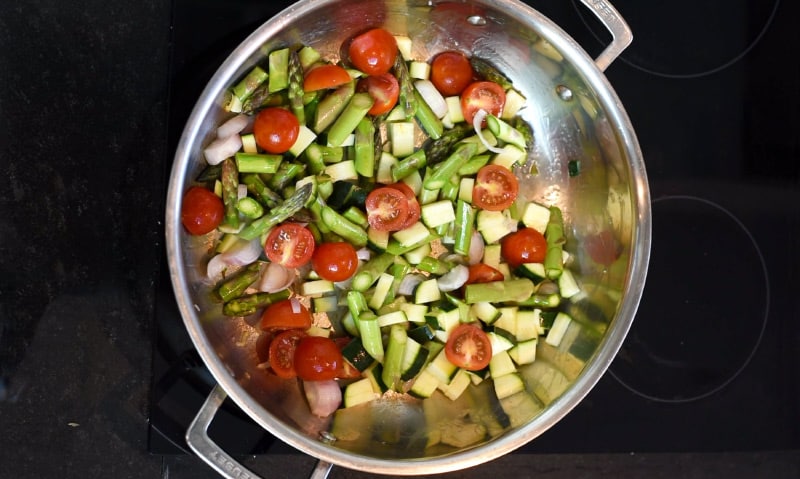 Chopped vegetables cooking in a large silver pan.