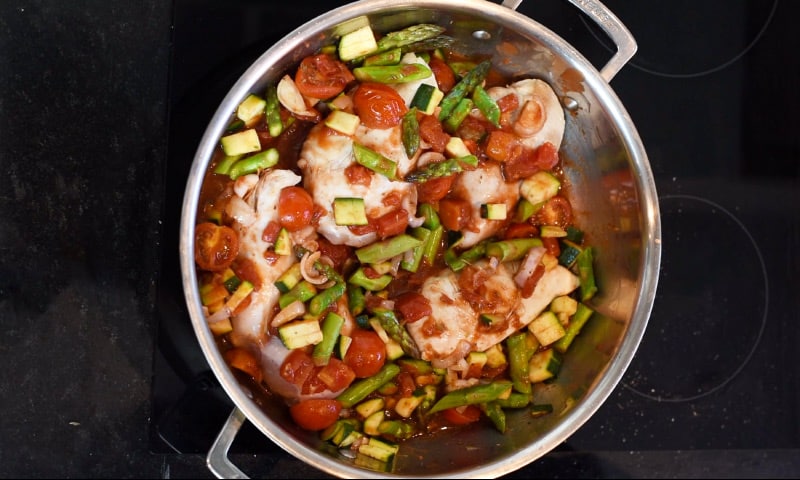 Chicken breasts and chopped vegetables in a large silver pan.