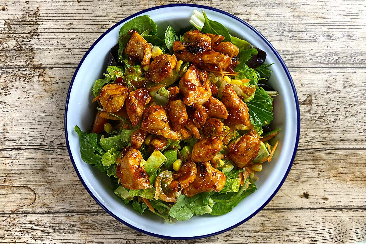 Barbecue chicken chunks on top of a bowl of salad.